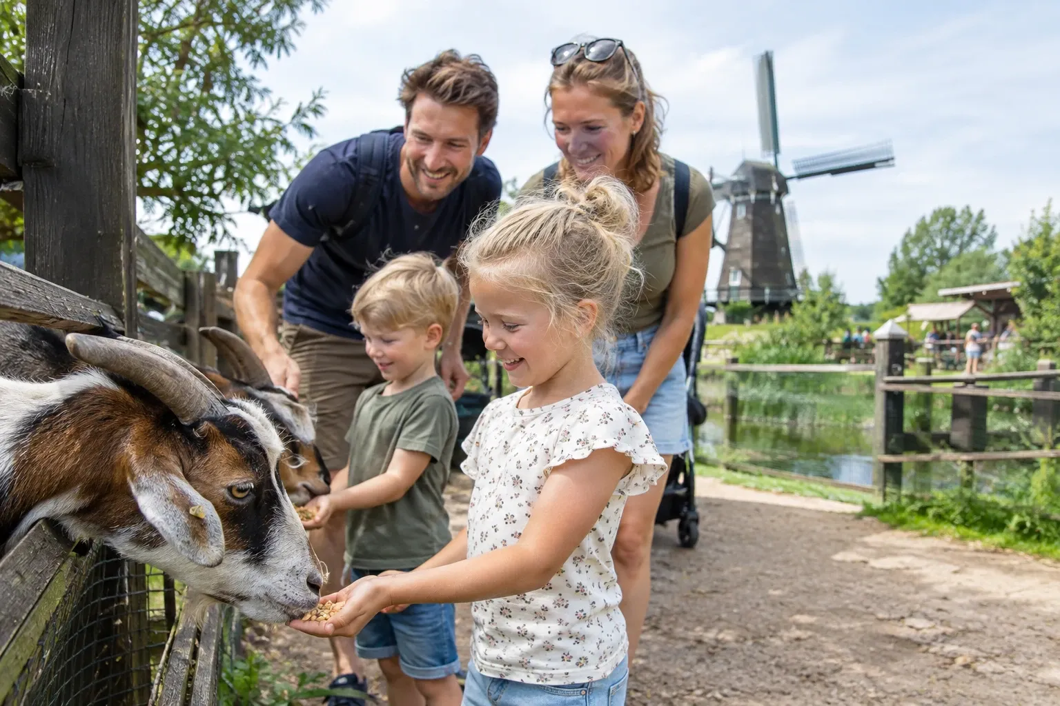 Kinderen voeren geiten bij een kinderboerderij, windmolen en ouders op achtergrond